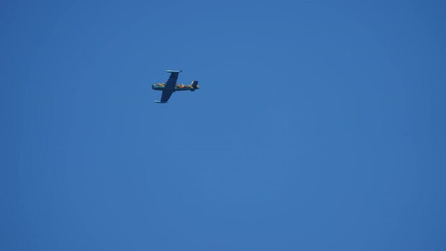 Single-engine military trainer with camouflage paint seen from below rolling through a clear bright blue sky during aerobatic display