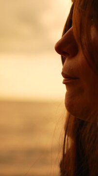 Woman profile sunset looking at the ocean during golden hour while talking in a peaceful contemplative mood