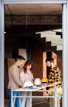 Adult couple discussing building plans with a contractor at a house construction site.