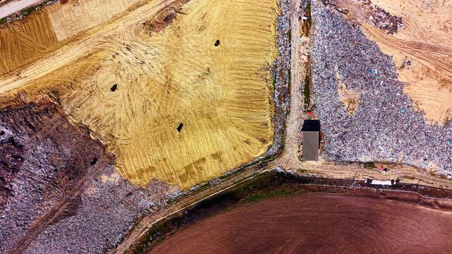 Abstract aerial composition splitting clean covered soil zones from active exposed plastic trash dumps. Top down view of waste cell segregation layout