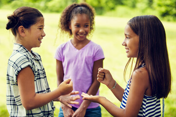 Fototapeta premium Children, game and park for rock, paper and scissors with smile, contest and bonding on summer break. Girl, kids and happy with friends, gesture or symbol with competition with laugh at playground