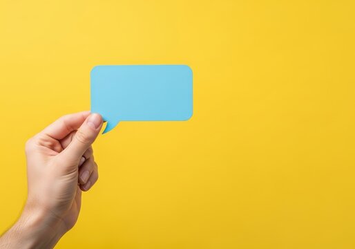 Hand Holding Blank Blue Speech Bubble Over Bright Yellow Background for Communication and Social Media Concept