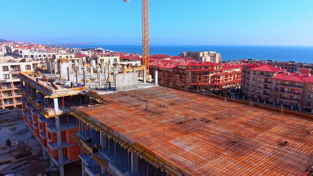 Drone shot showcasing rebar mesh installation on a multi story hotel project with red roofs in the background. Reinforced concrete floor slab of building under construction.