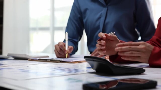 Business colleagues collaborating on financial reports, analyzing market data and charts during a team meeting, pointing to documents and discussing company strategy