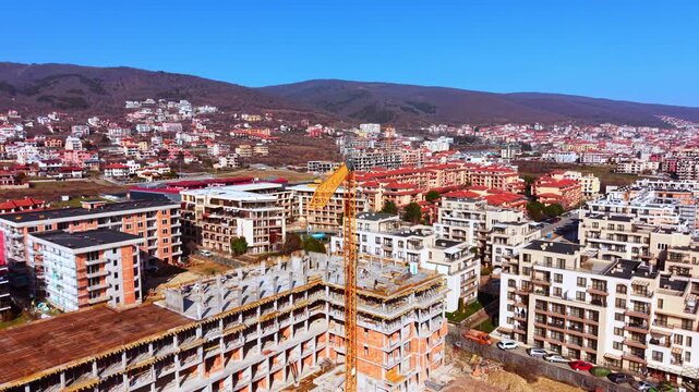 Drone view of modern brick and concrete resort blocks being developed near forested hills. Multi story apartment complex under construction in Sveti Vlas