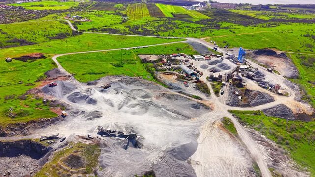 Aerial wide angle view of crushing machinery, aggregate stockpiles, conveyor belts and vibrant green fields. Drone perspective of gravel processing plant, Burgas, Bulgaria