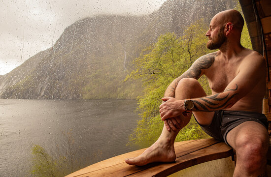 Man sitting in a sauna enjoying the view over the fjord