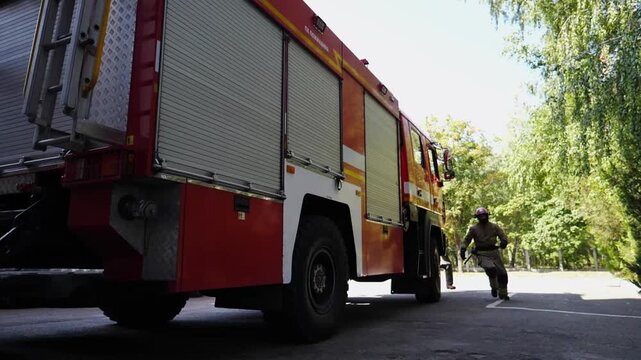 Young firefighters in uniform fast running for equipments to red truck. Professional male firemen getting ready to extinguish fire. Concept of saving lives and heroic profession. Close up Slow motion