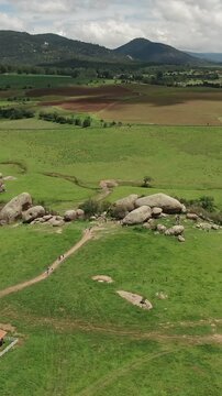 Vertical drone pullback reveal shot of Las Piedrotas granite boulders, tourists on hiking trails, meadows, and mountains in Tapalpa, Jalisco