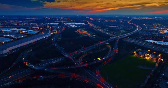 Top-down of a wide bridge spanning a multilane highway, New Jersey. Overhead of a long overpass crossing busy traffic lanes with curving ramps and red autumn woodland around