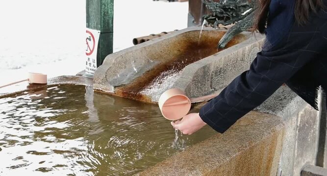 A person purifying hands with a ladle at Chozuya water pavilion in a Japanese shrine