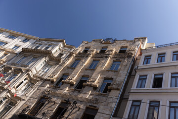 Fototapeta premium Upward view of a historic ornate stone building facades featuring carved details, decorative balconies and tall windows, lit by warm sunlight against a blue sky in an urban streetscape of Istanbul