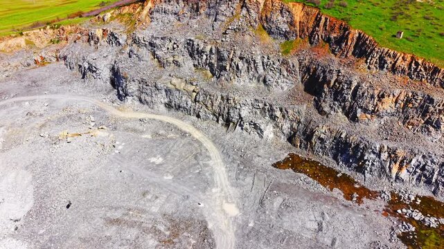 Detailed high angle perspective of layered stone cliffs with heavy machinery tracks on ground. Steep terraced rock face inside industrial quarry site.
