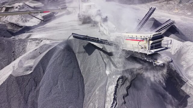 High angle view of mechanical arm discharging crushed stone onto a massive cone shaped stockpile. Close up aerial shot of conveyor belt tipping gravel.