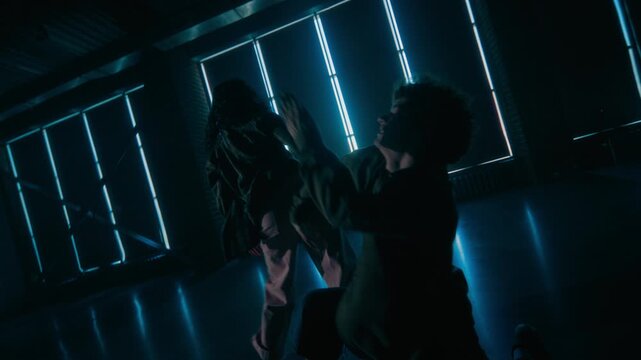 Cinematic shot of young man and woman as two young dancers performing fluid hip hop choreography in dark studio with angled camera movement