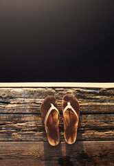 Obraz premium Sandals, black background and deck for travel, mockup space or holiday on vacation above. Wood jetty, flip flops and rustic pier for summer adventure, dark water and outdoor with top view of shoes