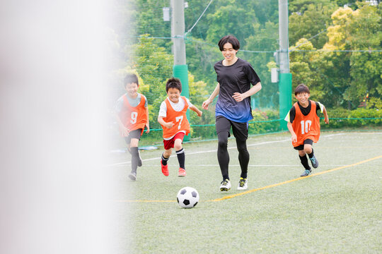 コーチと一緒にボールを追いかけるサッカー少年たち