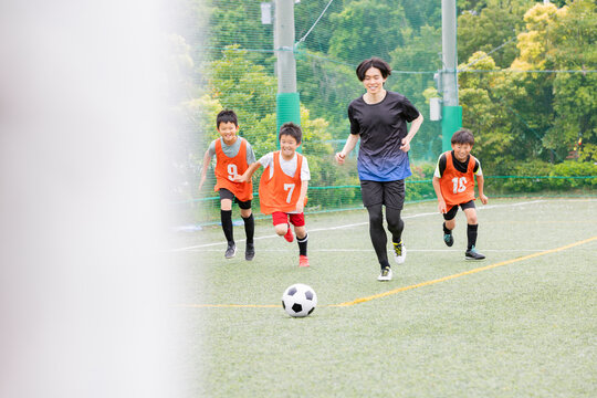 コーチと一緒にボールを追いかけるサッカー少年たち