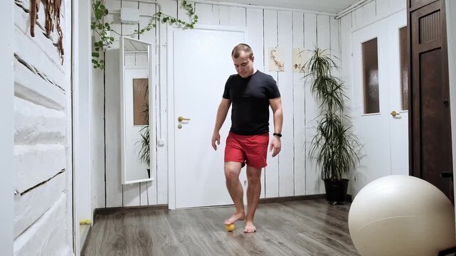 Barefeet man massaging the foot with spiky massage ball applying pressure to feet soles surface. The prickly yellow ball, treatment of flat feet. Person performs physical therapy exercises. 4K video.