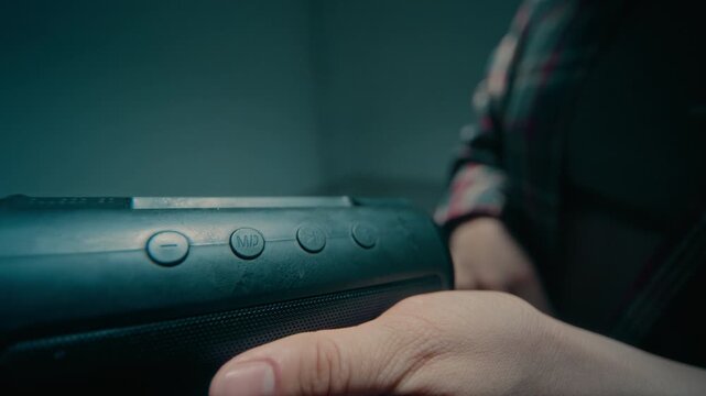 Cinematic close up shot of unrecognizable young man holding portable speaker in hand and pressing on button in slow motion, copy space