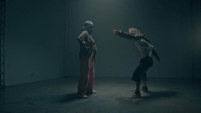 Cinematic zoom in shot of two dancers male and female facing each other during underground dance battle in dark industrial studio, copy space