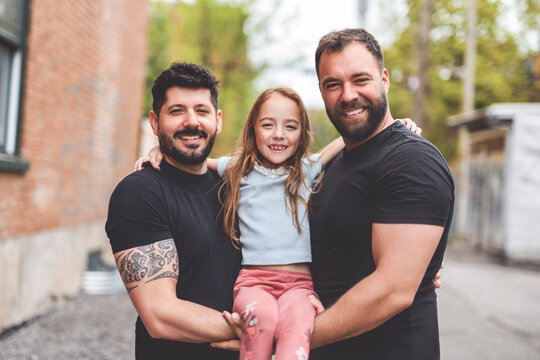 A Portrait of a happy gay couple outdoors in urban background with his adopt little girl