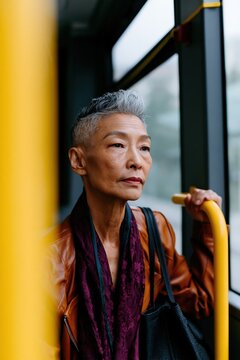 Stylish mature woman holding a bus pole looking out the window for urban commute lifestyle and public transport portrait for editorial use