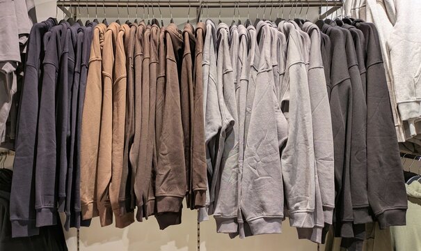 Grupo de sudaderas, ordenadas por colores, colgadas en un expositor de una boutique de ropa, vistas de perfil 