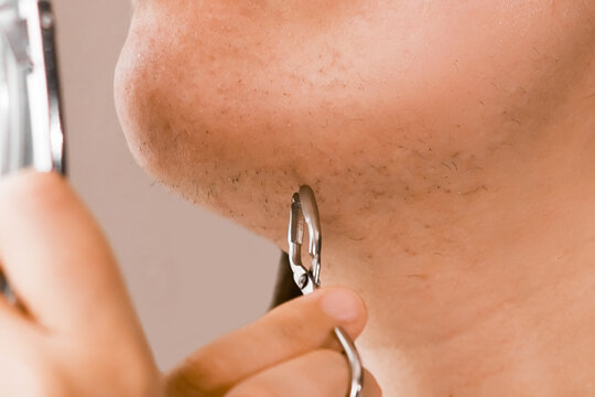 Close-up of unwanted facial hair removal from the chin using a tool during a home beauty routine, addressing hormonal changes and care.
