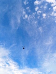 Fototapeta premium Silhouette of helicopter flying in clear blue sky with scattered white clouds. Minimalist aviation photo with copyspace for text overlay. Stock image for transportation, travel and freedom concepts.