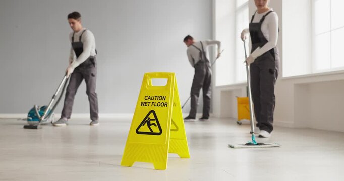 Cleaners and janitors mopping around caution sign. Uniformed workers and crew clean a bright interior using mops to maintain hygiene and prevent slips. Clear message of cleanliness and safety.