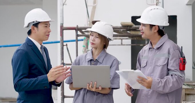 Asian female engineer uses laptop while male manager and contractor compare blueprint, reviewing construction document process, building progress, safety compliance, and project coordination.