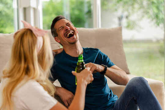 Friends Enjoy a Fun Time Laughing and Sharing Drinks Inside a Cozy Living Room During a Sunny Afternoon Gathering