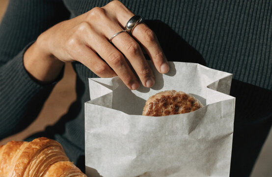 Woman holding a fresh chocolate chip cookie in a paper bag