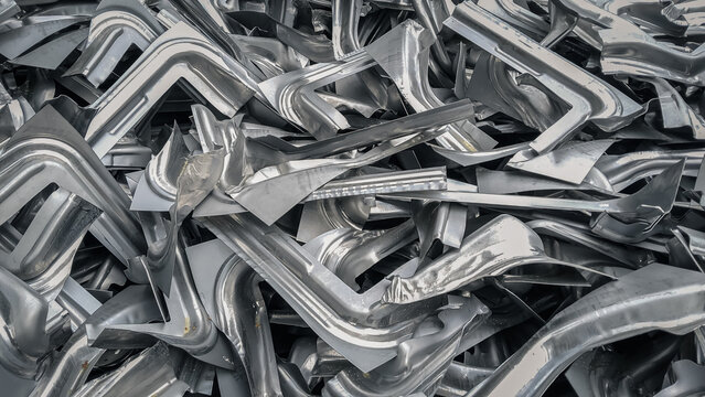 Pile of industrial scrap metal pieces from manufacturing press machine process. Shiny silver aluminum steel background texture.