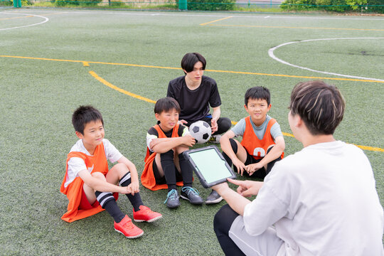 タブレットを使って作戦説明をするサッカーコーチと少年選手たち