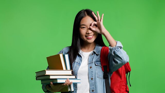 Young Asian student holding books and backpack on green screen background.