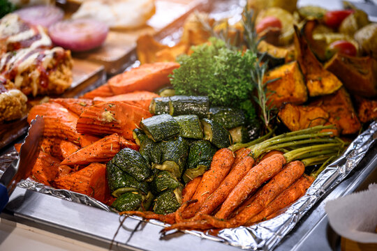 Close up of assorted roasted vegetables including carrots, pumpkins, and zucchinis seasoned with herbs on a catering buffet tray line