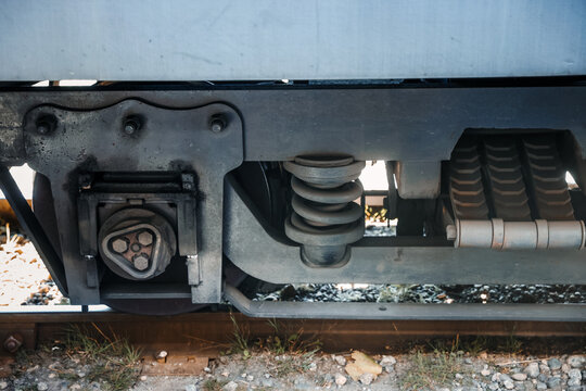 Close-up view of a locomotive train bogie assembly, showing the heavy mechanical suspension springs, axle box, and iron chassis on the railway track