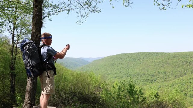 Middle-aged backpacker takes a cell phone snapshot of a scenic view from a mountaintop rocky outcrop vista
