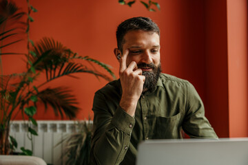 Bearded man working remotely with laptop and earbuds