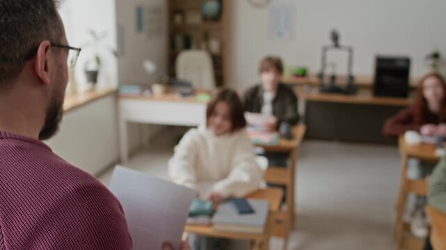 Close up over the shoulder shot of teacher in burgundy sweater teaching class in room equipped with 3D printers, while students listen intently