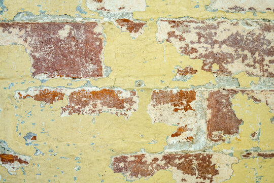 Close up view of rustic brick wall with peeling yellow paint.