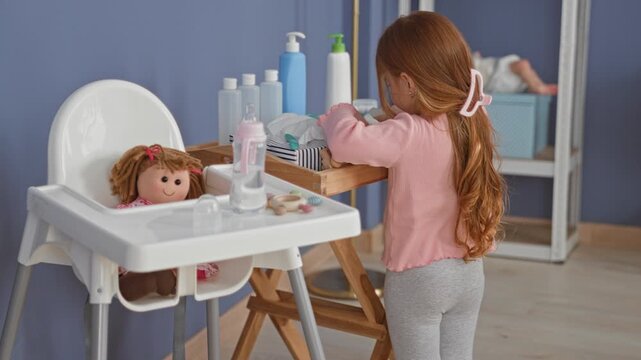 Girl reaches for a toy bottle and doll on a wooden play tray beside a highchair in a building; curious.