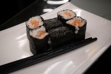 Assortimento di sushi maki giapponesi con salmone e avocado avvolti in alga nori serviti su un piatto bianco © Ilarialapreziosa