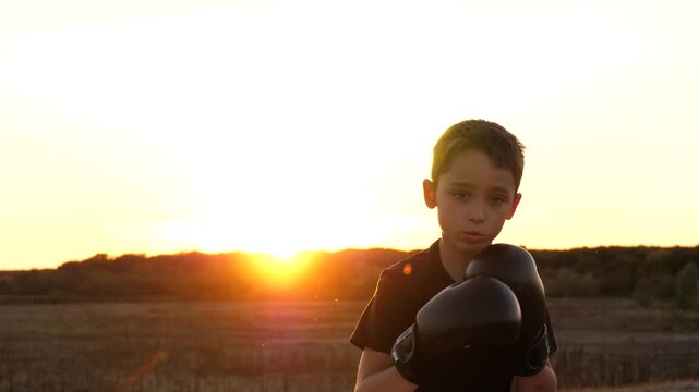 Young child boy boxing outdoors at sunset. Silhouette in warm light symbolizes resilience, inner strength and determination. Inspiring concept of overcoming challenges and personal growth.