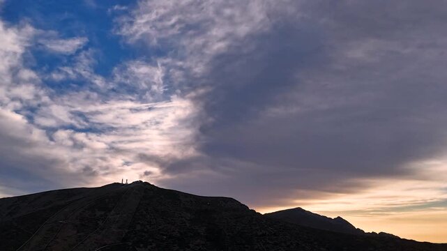 Aerial hyperlapse over La Bola del Mundo summit, Navacerrada, Madrid, Spain. Iconic peak in dramatic silhouette against turbulent fast moving cirrus and altocumulus clouds at dusk.