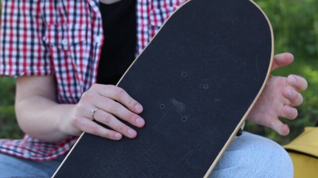 Girl spins wheels on skateboard checking their serviceability. Teenager preparing to ride, examining details of her first skateboard. Close-up of hands and skate outdoors. Skateboard inspection