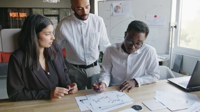 Three coworkers engage in a meeting at their office to learn about financial markets and discuss trading strategies. The diverse group works together to analyze data and share insights