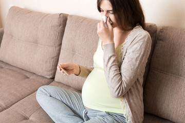 Obraz premium Sick pregnant woman blowing nose into tissue at home Healthy millennial healthcare concept